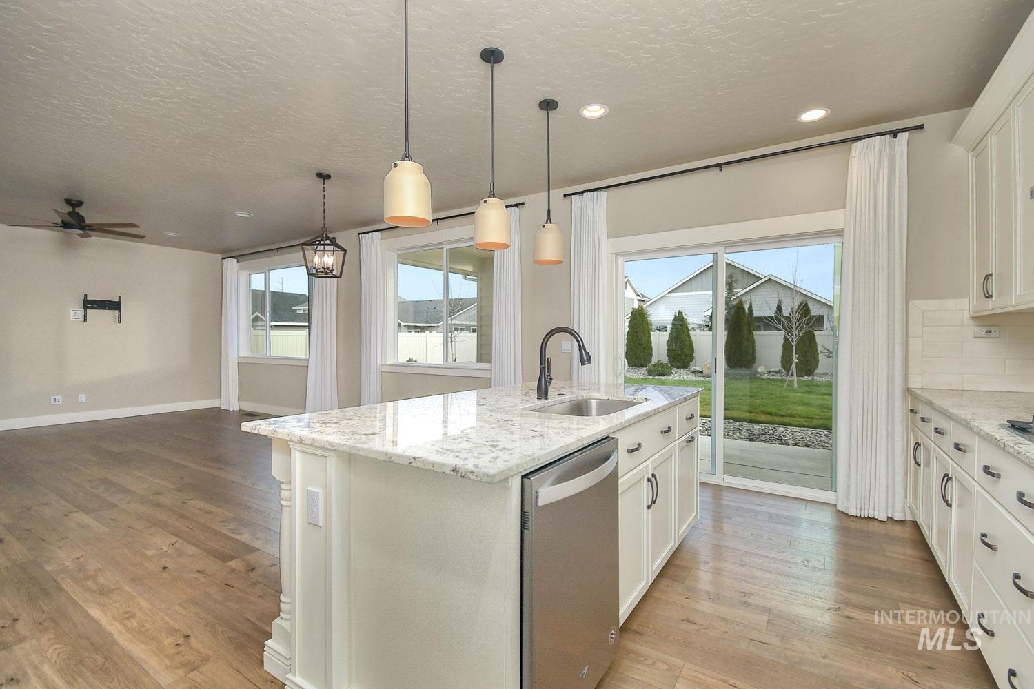 5771 West Daphne Drive Meridian, ID 83646 - Photo 15 of 32 Kitchen featuring stainless steel dishwasher, white cabinets, light stone countertops, an island with sink, and a textured ceiling