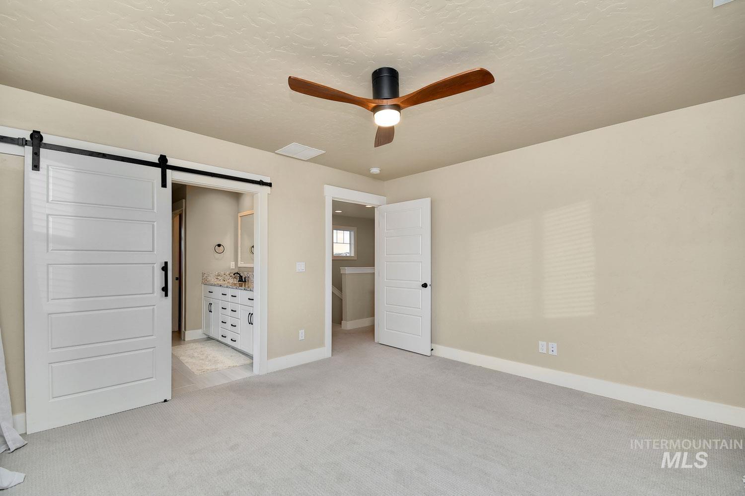 5771 West Daphne Drive Meridian, ID 83646 - Photo 19 of 32 Unfurnished bedroom featuring ensuite bathroom, a ceiling fan, a barn door, light carpet, and a textured ceiling