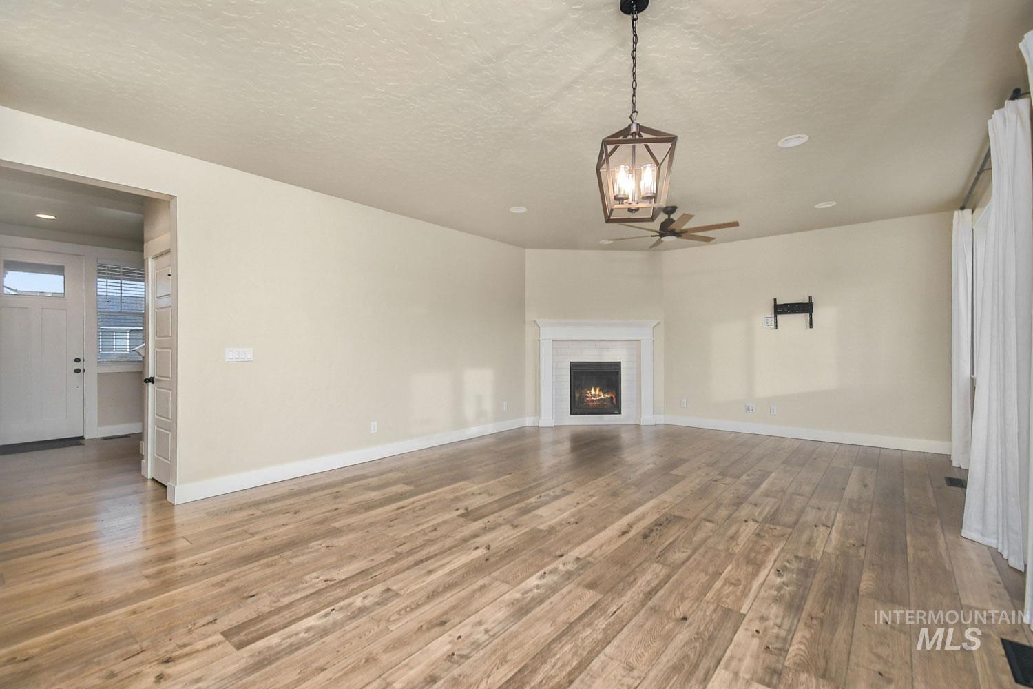 5771 West Daphne Drive Meridian, ID 83646 - Photo 8 of 32 Unfurnished living room featuring a lit fireplace, light wood-style floors, a textured ceiling, and a ceiling fan
