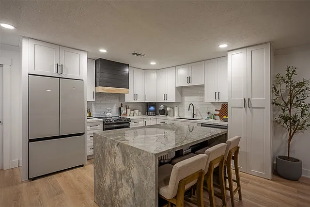 a kitchen with stainless steel appliances granite countertop a refrigerator a sink a stove a dining table and chairs