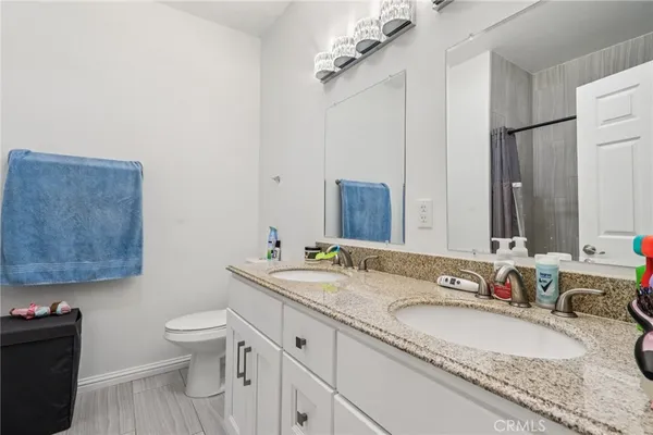 a bathroom with a granite countertop double vanity sink a mirror and a toilet