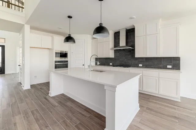 a kitchen with stainless steel appliances granite countertop a sink a microwave a refrigerator and white cabinets with wooden floor