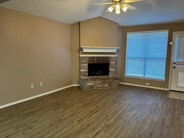a view of an empty room with wooden floor fireplace and a window