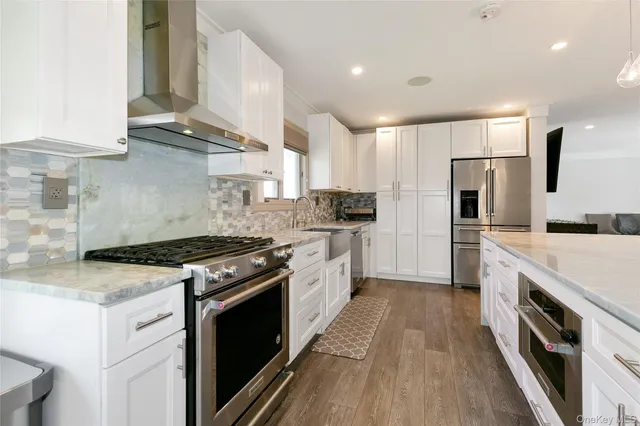a kitchen with stainless steel appliances granite countertop a stove top oven a sink dishwasher a refrigerator and white cabinets with wooden floor