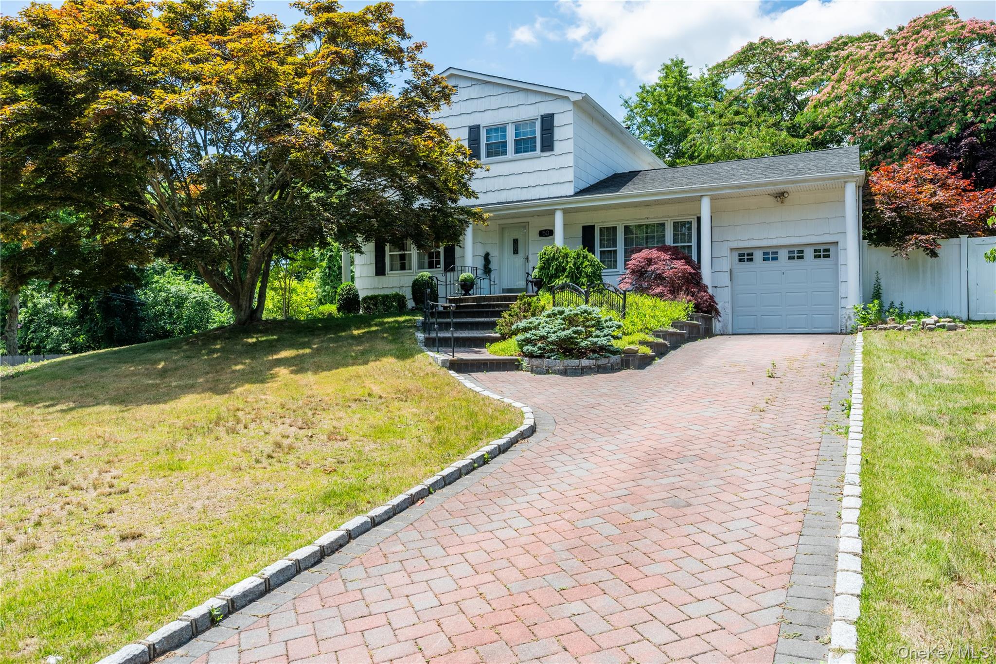 50 Propose Road Shirley, NY 11967 - Photo 1 of 12 White two-story residence featuring a front-facing garage, a brick paver driveway, and a covered porch entry.