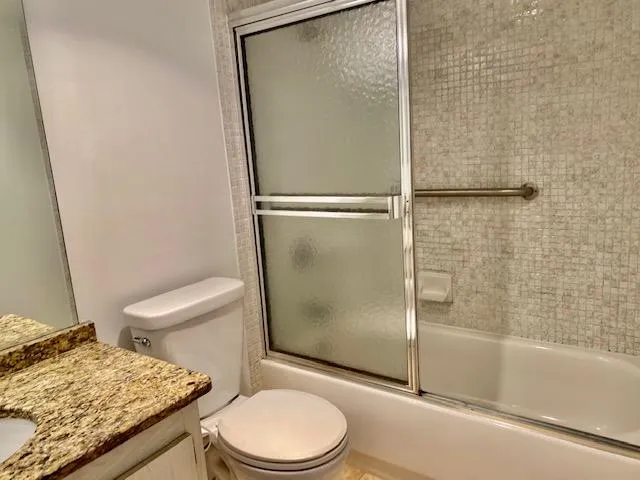 a bathroom with a granite countertop bathtub shower and toilet
