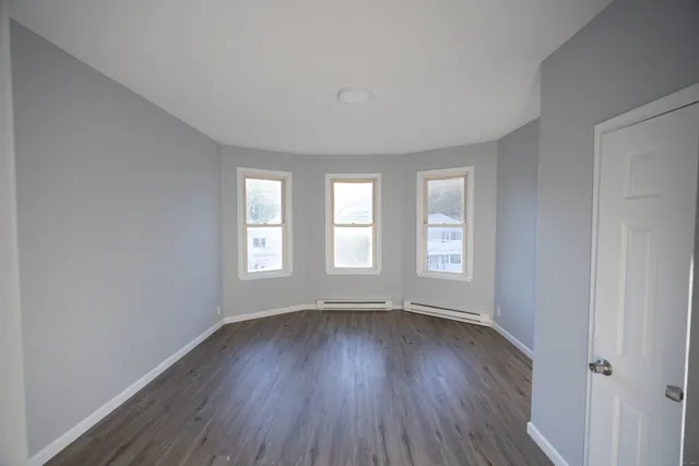 a view of an empty room with wooden floor and window