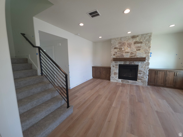 1267 West 2350 South Perry, UT 84302 - Photo 2 of 20 Living area featuring a stone fireplace with a wood mantle, built-in wood cabinetry, wood-finish flooring, recessed lighting, and a staircase with a black metal railing