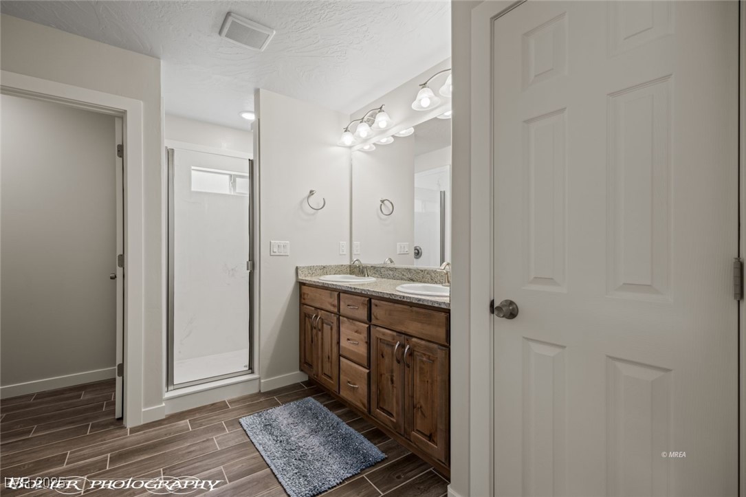 942 Shadow Hawk Ridge Mesquite, NV 89027 - Photo 39 of 67 Full bath with wood tiled floors, baseboards, double vanity, a shower stall, and a textured ceiling