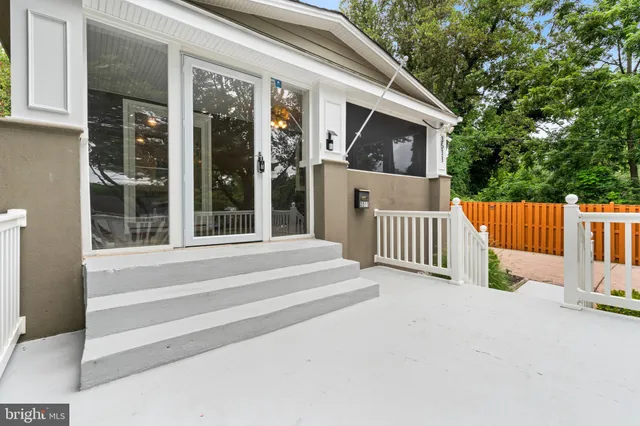 a view of a house with a small yard and wooden fence and large trees