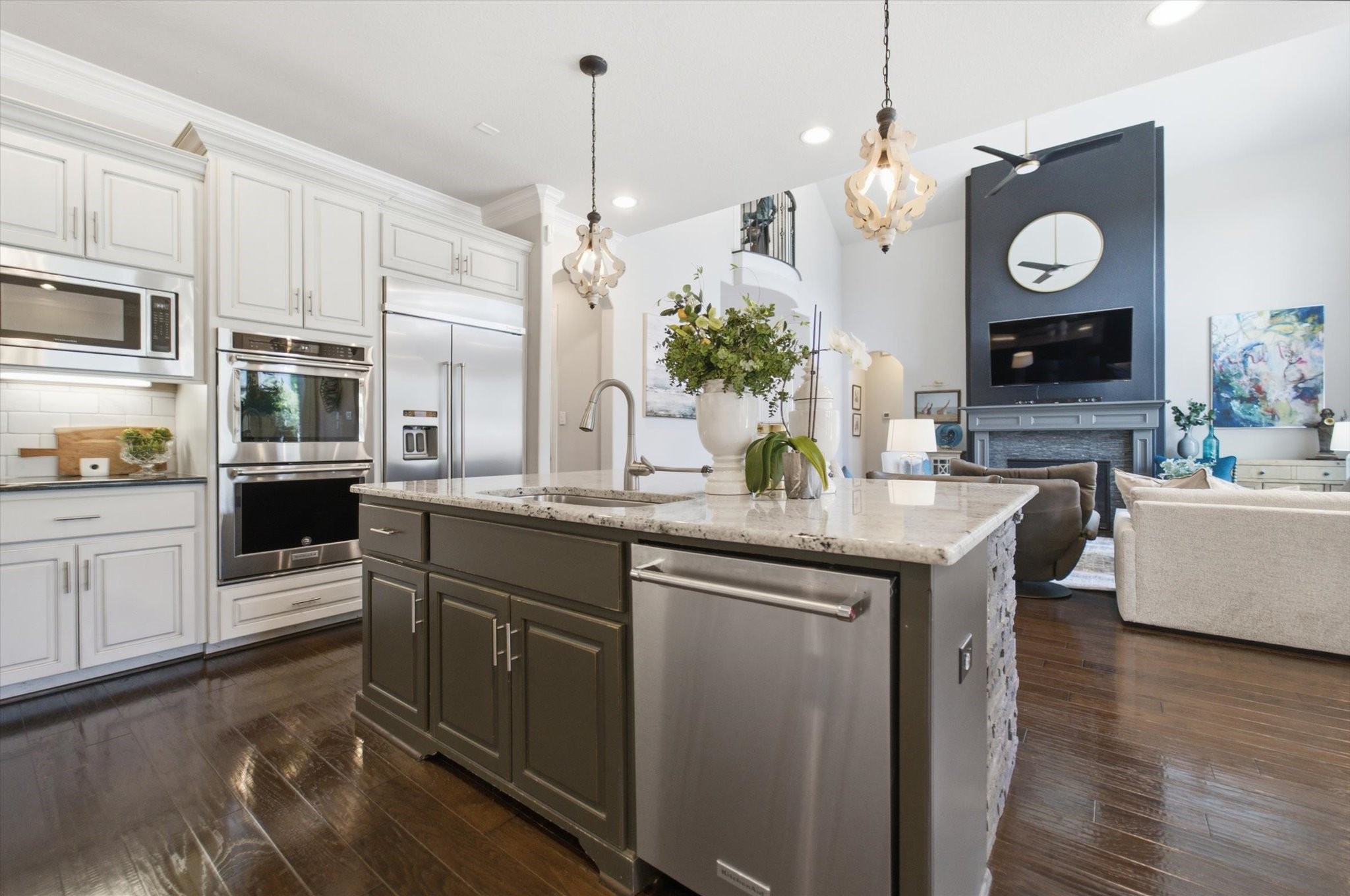 23722 Thortons Park Lane Spring, TX 77389 - Photo 26 of 48 This open-concept space features a modern kitchen with stainless steel appliances, a large island with granite countertops, and elegant pendant lighting. It seamlessly flows into a stylish living area with a high ceiling, a contemporary fireplace, and a mounted TV, creating a perfect setting for entertaining.