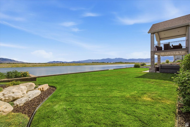 21 Pier Place Tooele, UT 84074 - Photo 95 of 112 Expansive waterfront backyard featuring a manicured lawn, stone landscaping, a covered patio, and an upper-level balcony