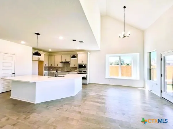 a view of kitchen with kitchen island stainless steel appliances wooden floor cabinets and a window