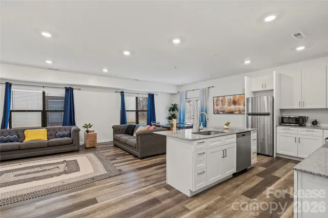 a large white kitchen with stainless steel appliances granite countertop a couch and a view of living room