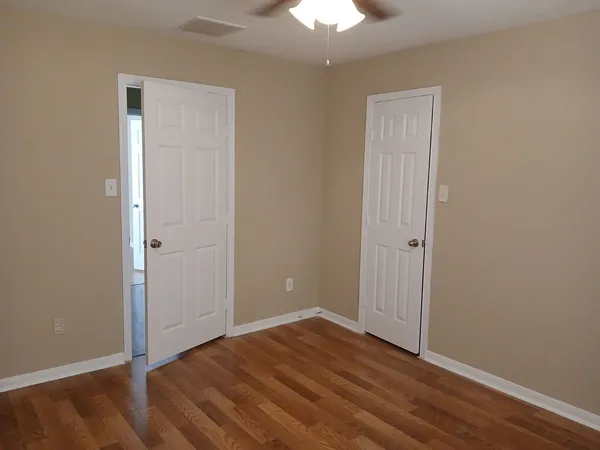 a view of an empty room with wooden floor and a chandelier fan