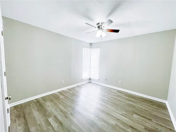 a view of an empty room with wooden floor and a ceiling fan