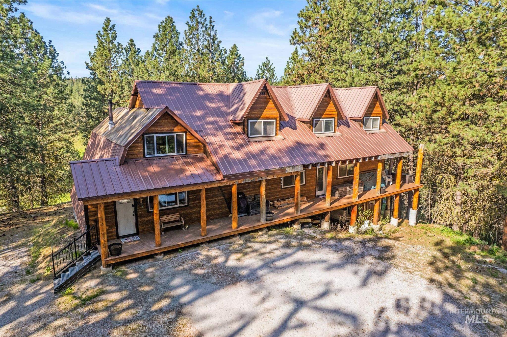 Wood-sided home featuring a wrap-around porch supported by log columns, a metal roof, and multiple dormer windows