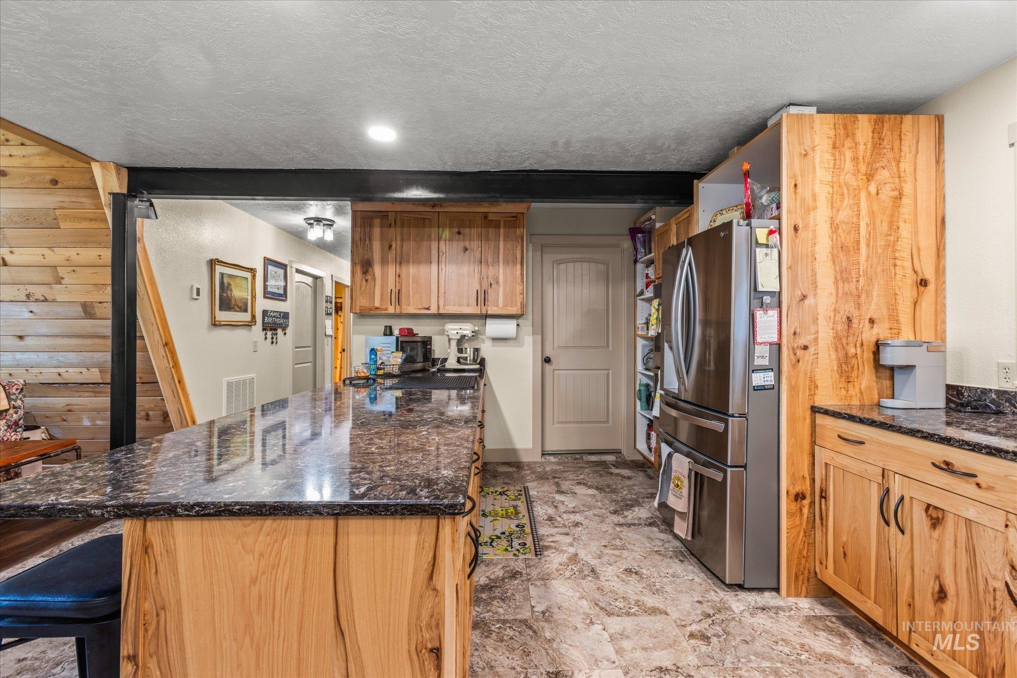 1 Sunset Trail Banks, ID 83602 - Photo 12 of 42 Kitchen featuring wood cabinetry, dark speckled countertops, tile flooring, and a stainless steel refrigerator