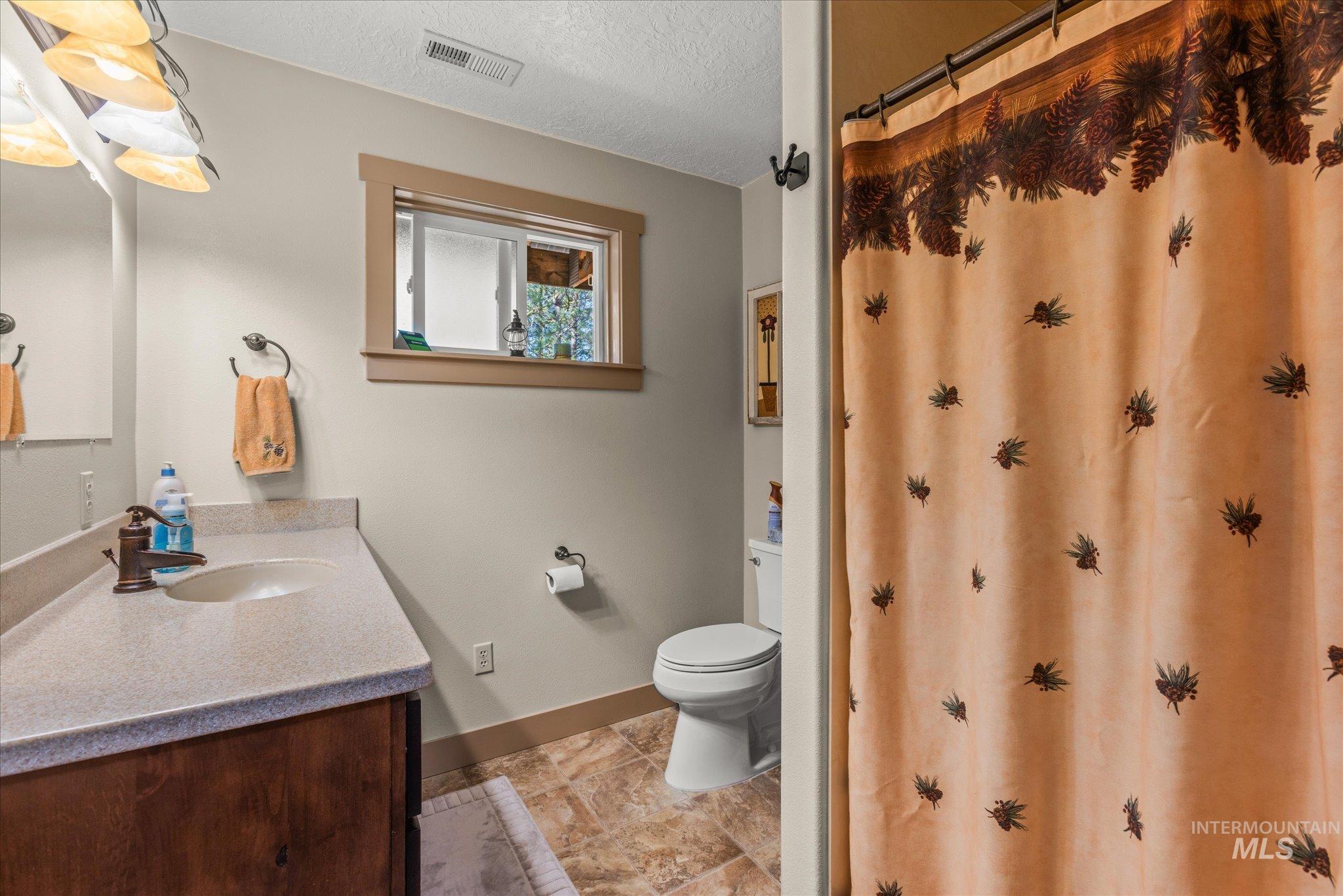 1 Sunset Trail Banks, ID 83602 - Photo 15 of 42 Bathroom featuring a wood-finish vanity with an integrated sink, a light-colored countertop, a window with wood trim, and textured floor tiles