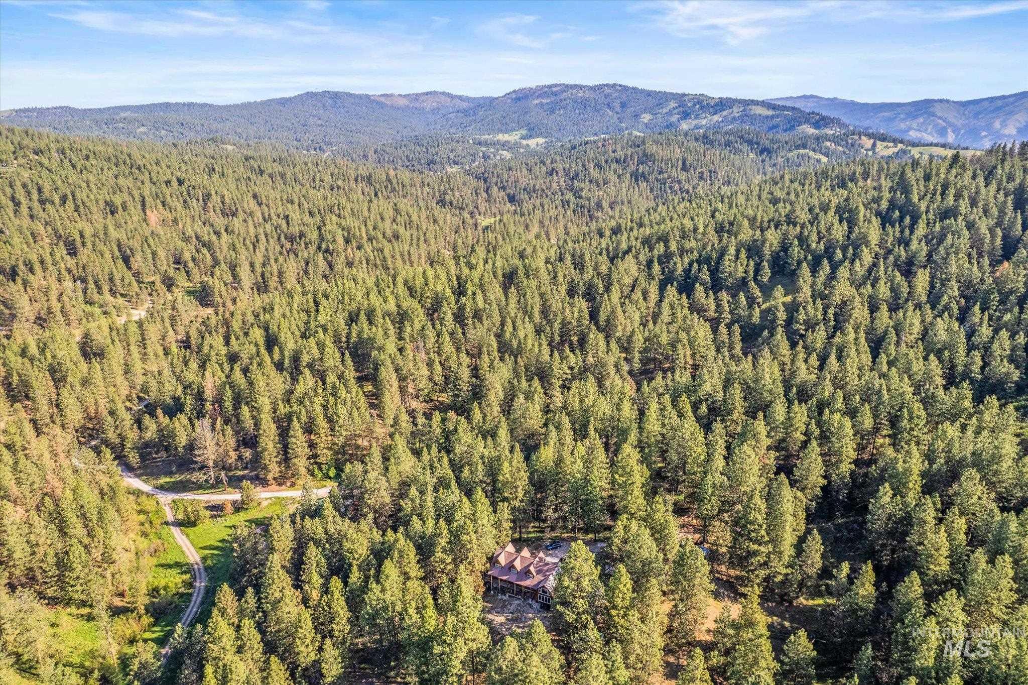 1 Sunset Trail Banks, ID 83602 - Photo 40 of 42 Mountain property featuring a house set amidst dense evergreen forests, a winding unpaved road, and distant mountain ranges