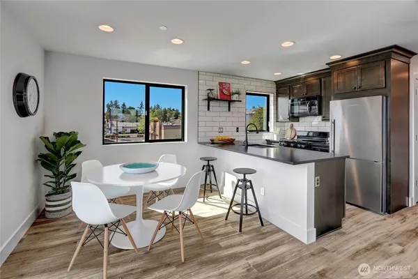 a kitchen with stainless steel appliances a refrigerator a stove a dining table and chairs with wooden floor
