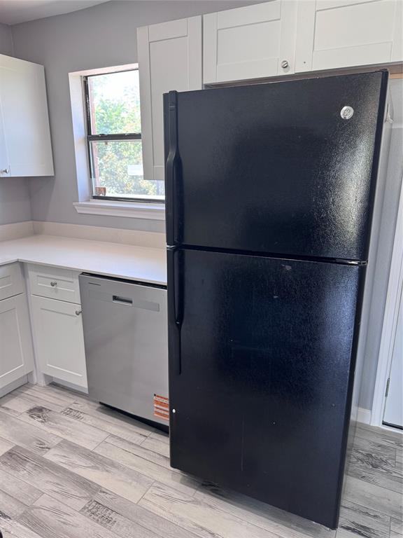 1736 Ransom Terrace Fort Worth, TX 76112 - Photo 5 of 27 Kitchen featuring a black top-freezer refrigerator, stainless steel dishwasher, white shaker-style cabinetry, light-toned countertops, and wood-finish flooring