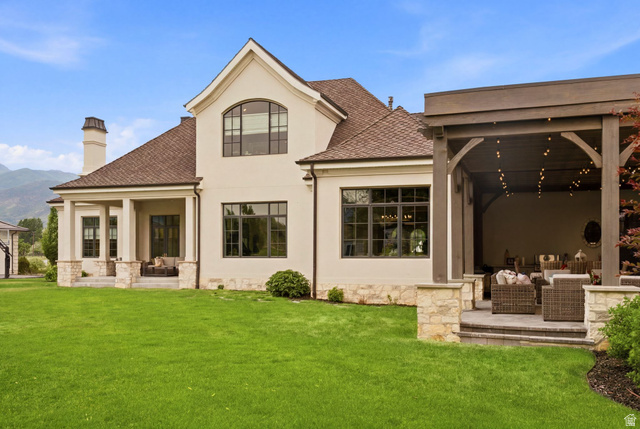 71 Farm Road Midway, UT 84049 - Photo 90 of 92 Expansive rear exterior featuring a covered patio with integrated lighting, a separate covered porch, a stucco and stone facade, dark-framed windows, and a manicured lawn