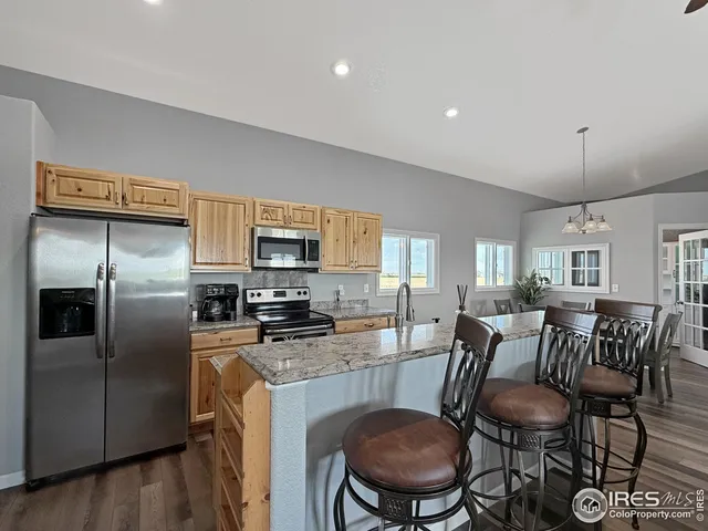 a kitchen with stainless steel appliances granite countertop a refrigerator a stove a sink a dining table and chairs with wooden floor