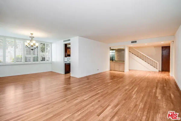 a view of empty room with wooden floor and kitchen view