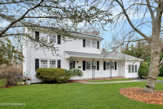 a view of a white house with a big yard and potted plants and large trees