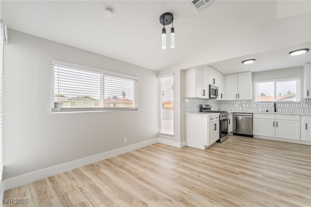 652 Red Lake Way Las Vegas, NV 89110 - Photo 12 of 66 Kitchen featuring white cabinetry, stainless steel appliances, backsplash, vaulted ceiling, and light wood-style floors