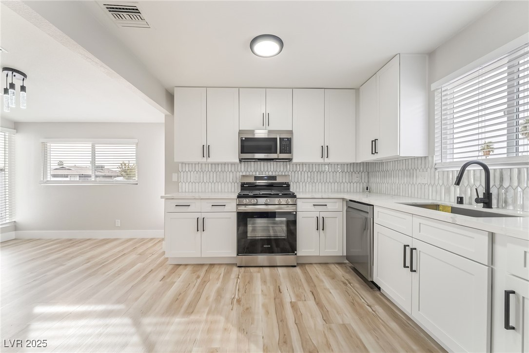 652 Red Lake Way Las Vegas, NV 89110 - Photo 8 of 66 Kitchen with stainless steel appliances, white cabinetry, light wood finished floors, light stone counters, and backsplash