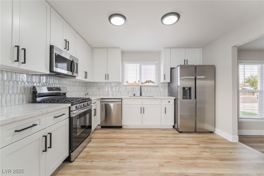 652 Red Lake Way Las Vegas, NV 89110 - Photo 9 of 66 Kitchen with stainless steel appliances, white cabinetry, light stone countertops, backsplash, and light wood-type flooring