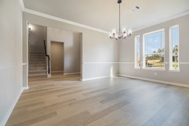 an empty room with wooden floor chandelier and windows
