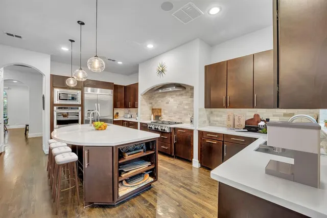 a kitchen with stainless steel appliances kitchen island granite countertop a sink a stove and a wooden floors
