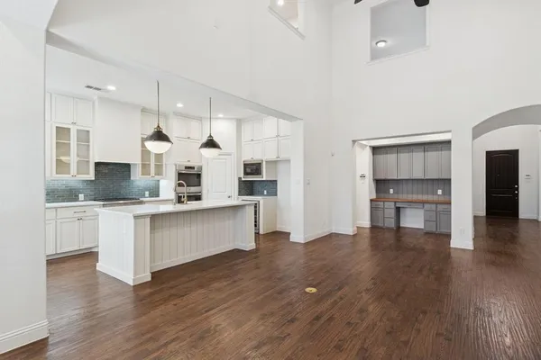 a large white kitchen with a refrigerator a sink dishwasher a stove and white cabinets with wooden floor