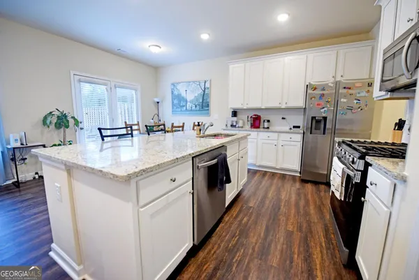 a kitchen with kitchen island wooden floors white appliances a sink and living room view