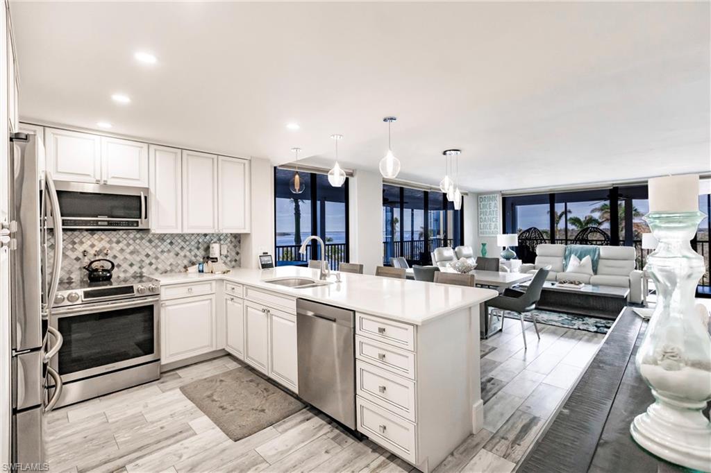 Kitchen with sink, kitchen peninsula, hanging light fixtures, white cabinetry, and stainless steel appliances