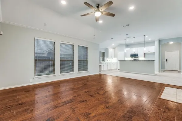 a view of an empty room with wooden floor and a kitchen