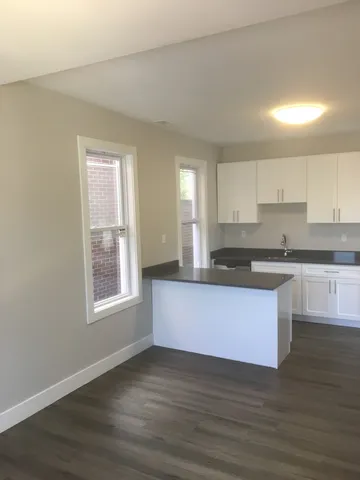 a large kitchen with stainless steel appliances granite countertop a stove a sink a refrigerator and white cabinets with wooden floor