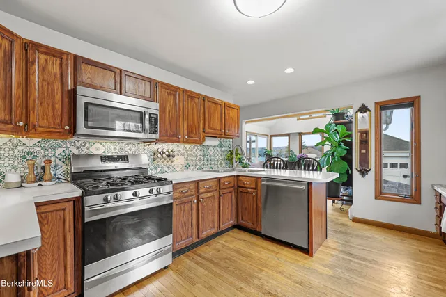 a kitchen with stainless steel appliances granite countertop wooden cabinets a stove top oven a sink and dishwasher with wooden floor