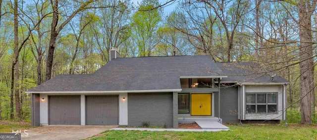 a view of a brick house with a yard plants and large tree