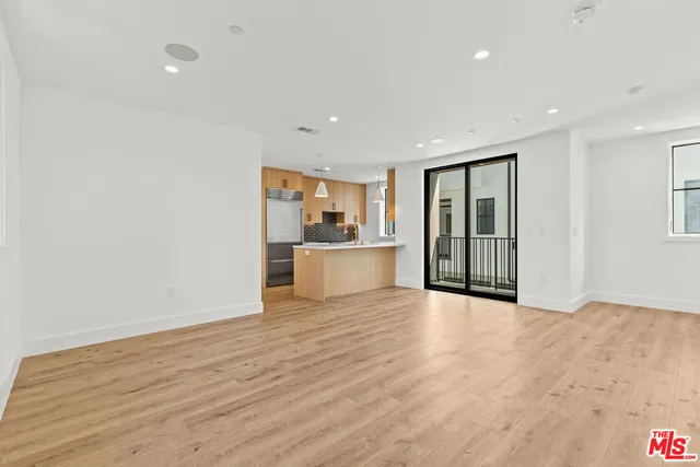 a view of an empty room with wooden floor and a kitchen