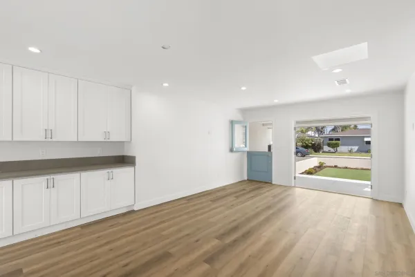 a view of an empty room with kitchen and window
