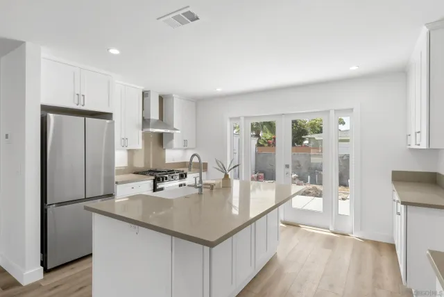 a kitchen with stainless steel appliances granite countertop a refrigerator a sink a stove and white cabinets with wooden floor