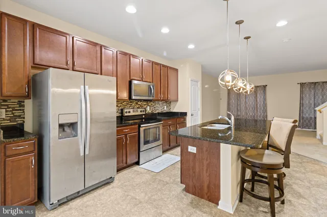 a kitchen with stainless steel appliances granite countertop a refrigerator a stove a sink a dining table and chairs with wooden floor