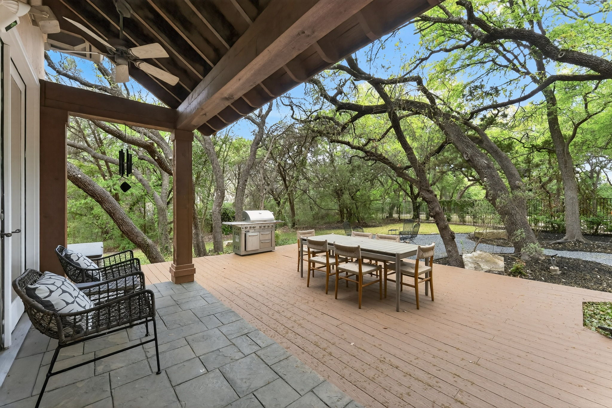 4110 Bunny Run, Unit 3 Austin, TX 78746 - Photo 29 of 35 The property features an expansive covered outdoor patio with a ceiling fan, a wooden deck, and a tiled area, overlooking a lush, wooded landscape