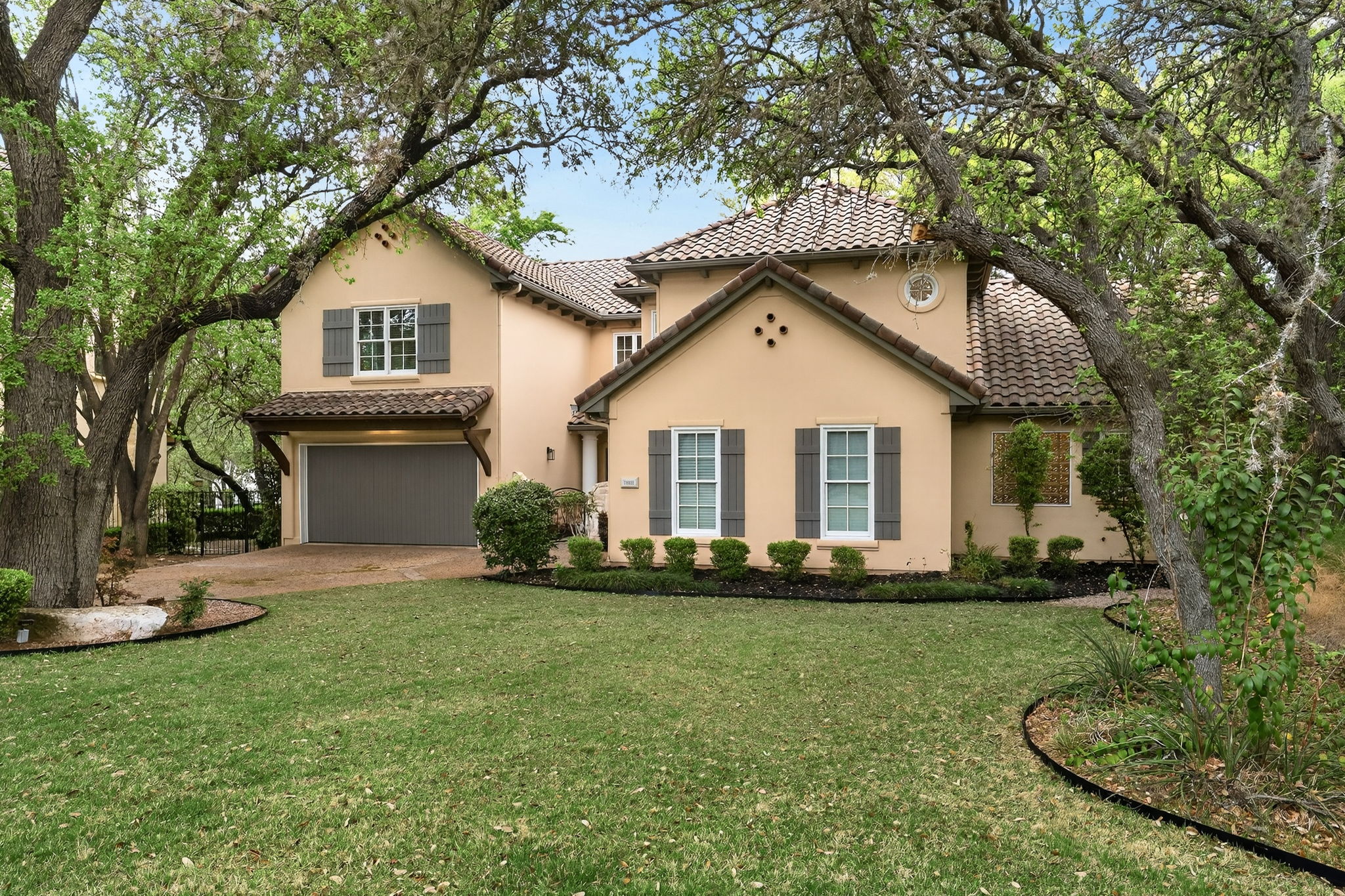4110 Bunny Run, Unit 3 Austin, TX 78746 - Photo 3 of 35 The property features a stucco exterior, a tiled roof, and a prominent front yard with a well-maintained lawn and mature trees