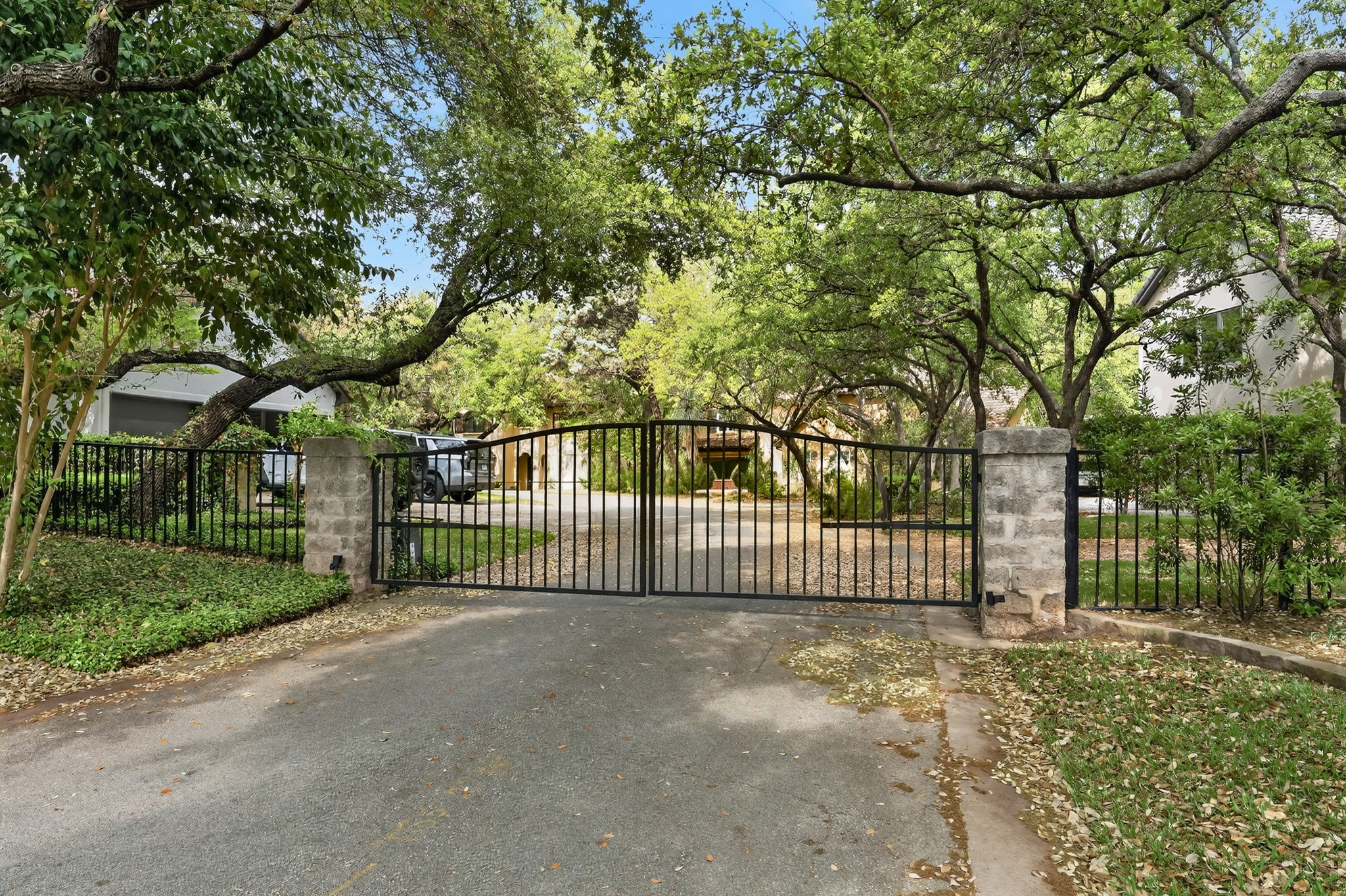 4110 Bunny Run, Unit 3 Austin, TX 78746 - Photo 34 of 35 The property features a gated entrance with black metal gates and stone pillars, surrounded by mature trees and lush greenery