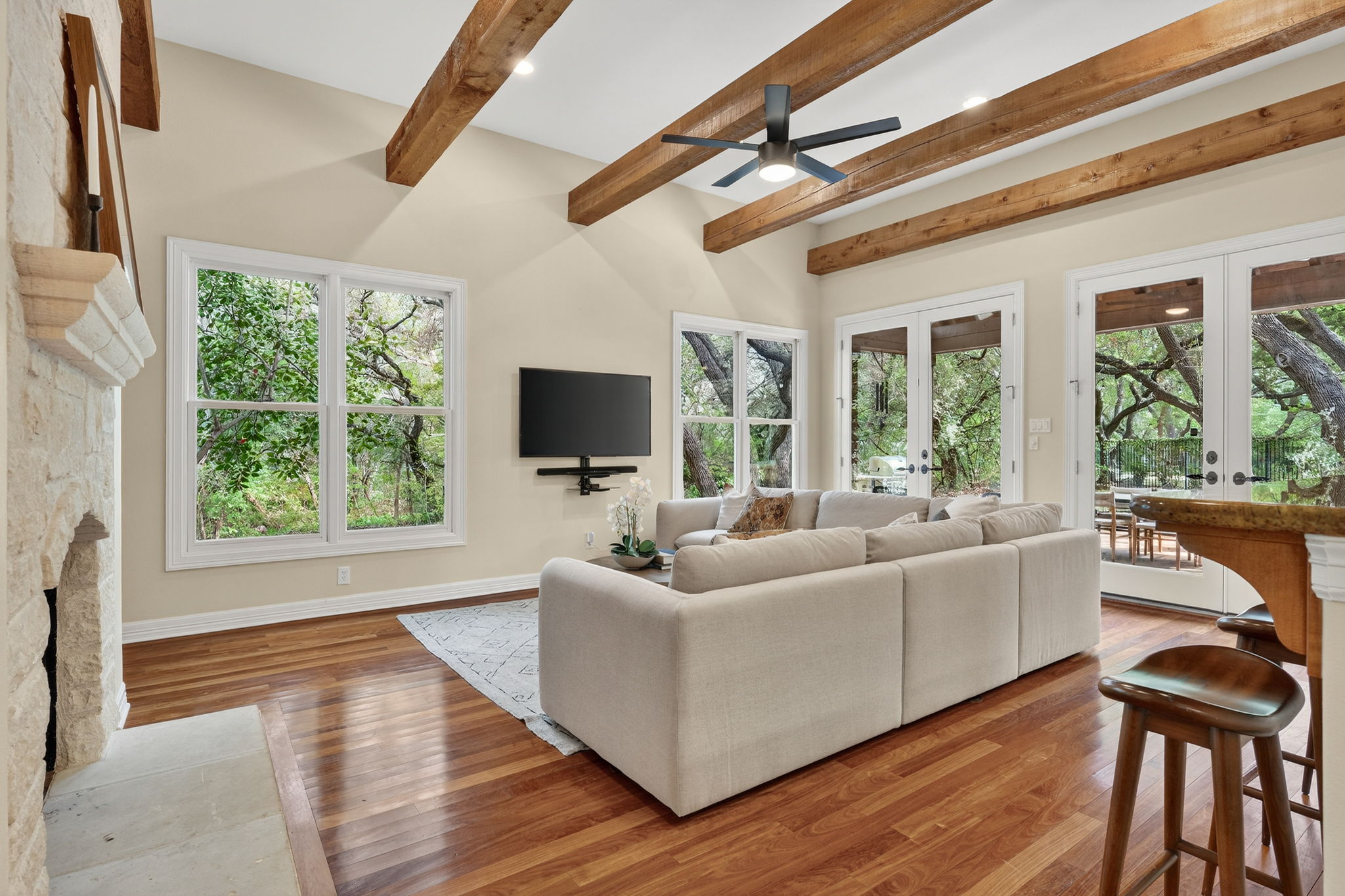 4110 Bunny Run, Unit 3 Austin, TX 78746 - Photo 9 of 35 Living area featuring hardwood flooring, exposed ceiling beams, a stone fireplace, and large windows and glass-paneled doors providing natural light